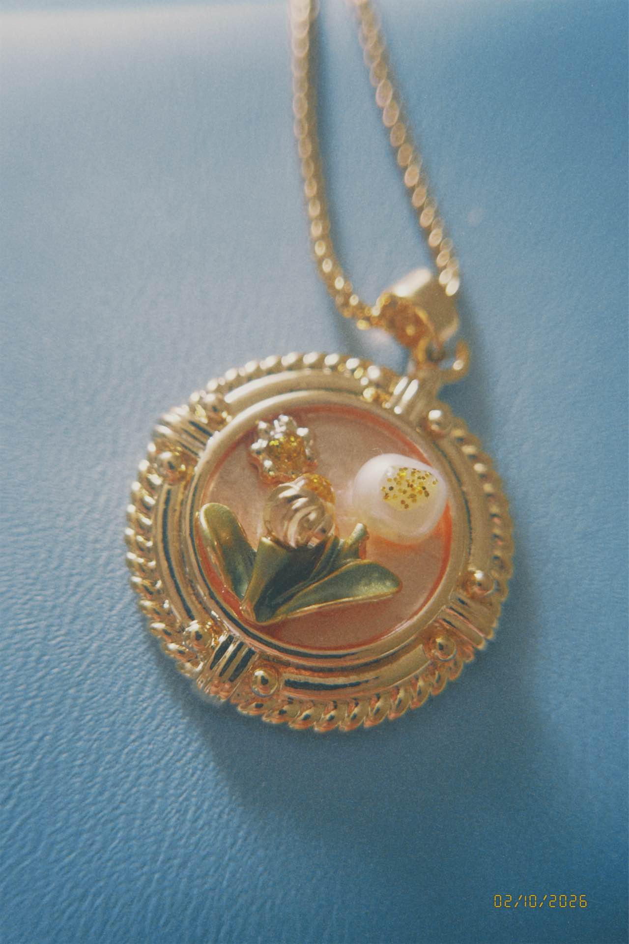 Gold necklace with a round pendant featuring a floral design on a light blue background.
