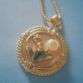 Gold necklace with a round pendant featuring a floral design on a light blue background.