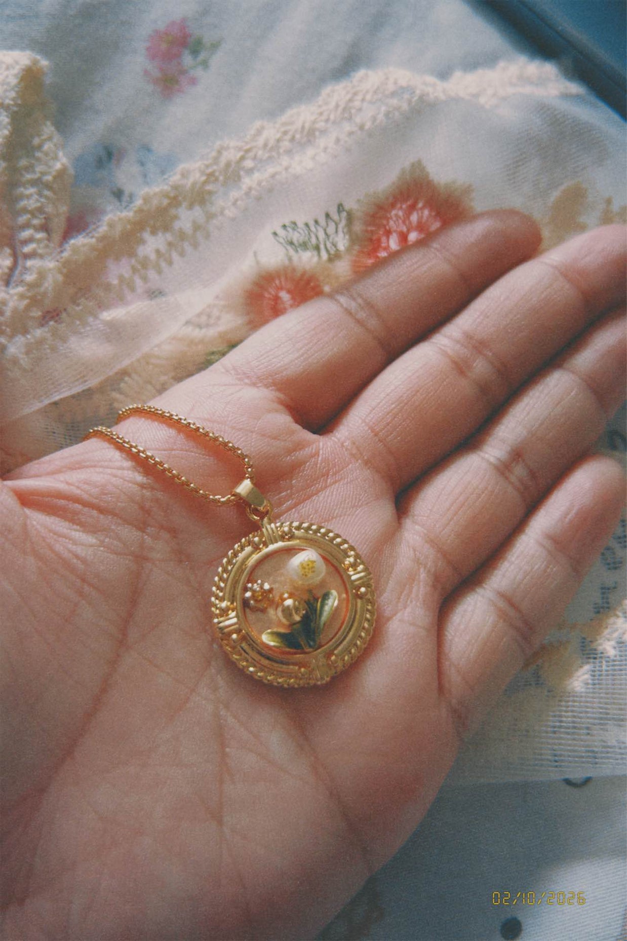 Gold pendant held in a hand with a floral-patterned fabric background