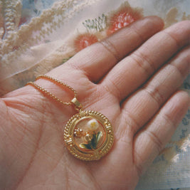 Gold pendant held in a hand with a floral-patterned fabric background