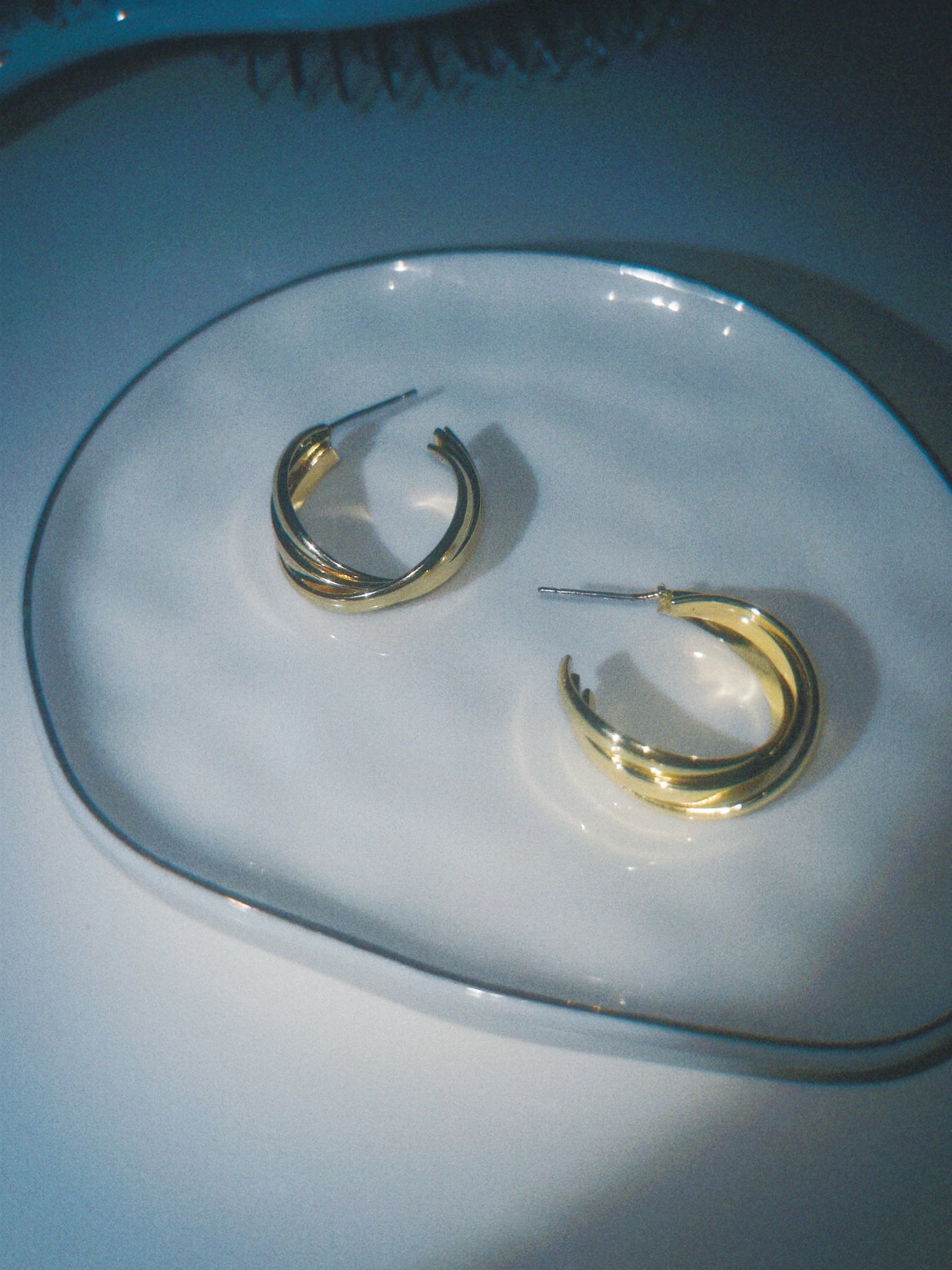 Gold hoop earrings on a clear glass plate with a blue background