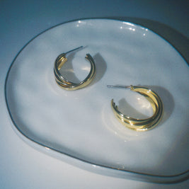 Gold hoop earrings on a clear glass plate with a blue background