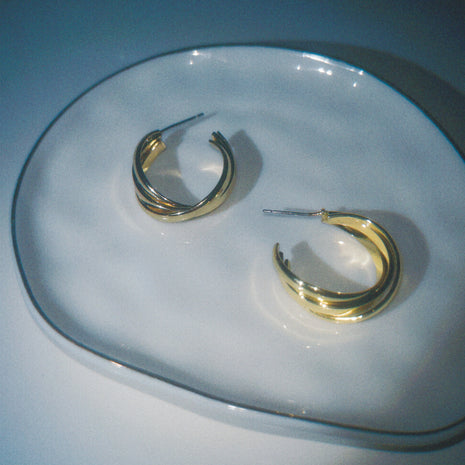 Gold hoop earrings on a clear glass plate with a blue background