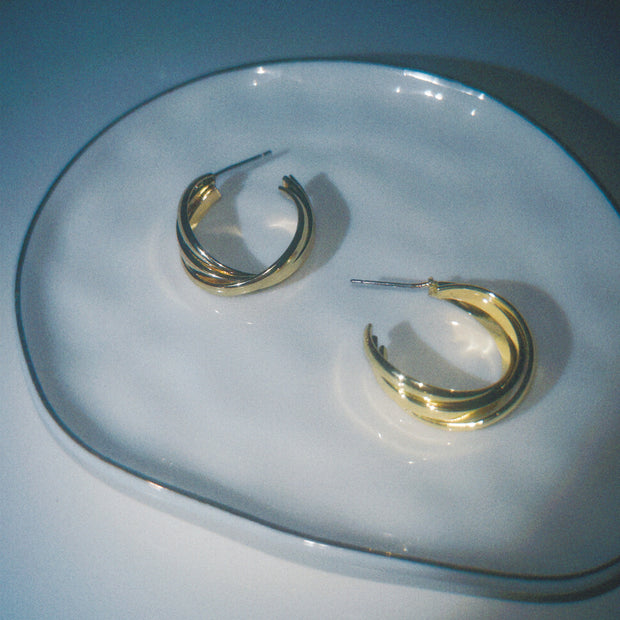 Gold hoop earrings on a clear glass plate with a blue background