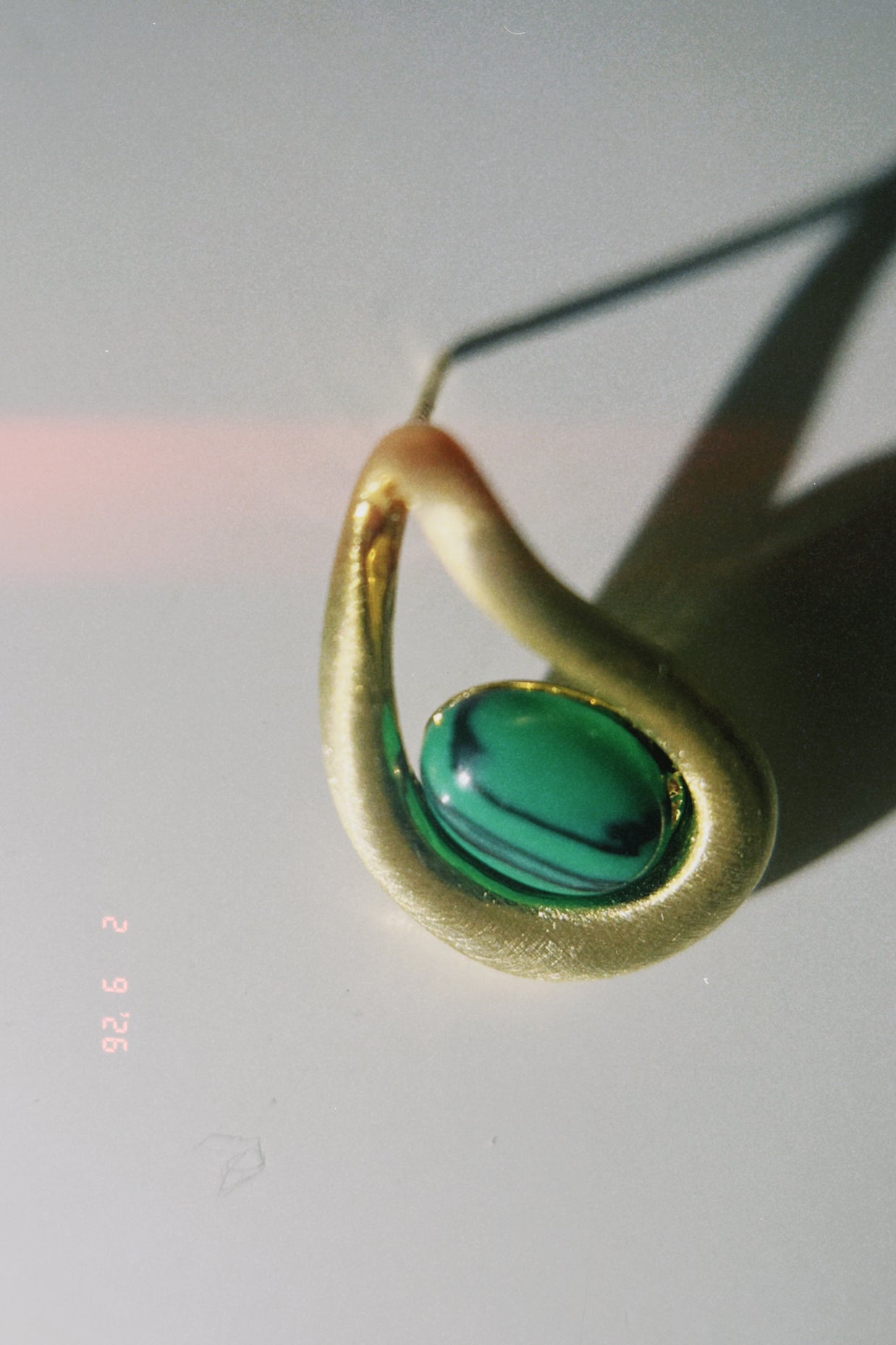Gold earring with a green gemstone on a light gray background