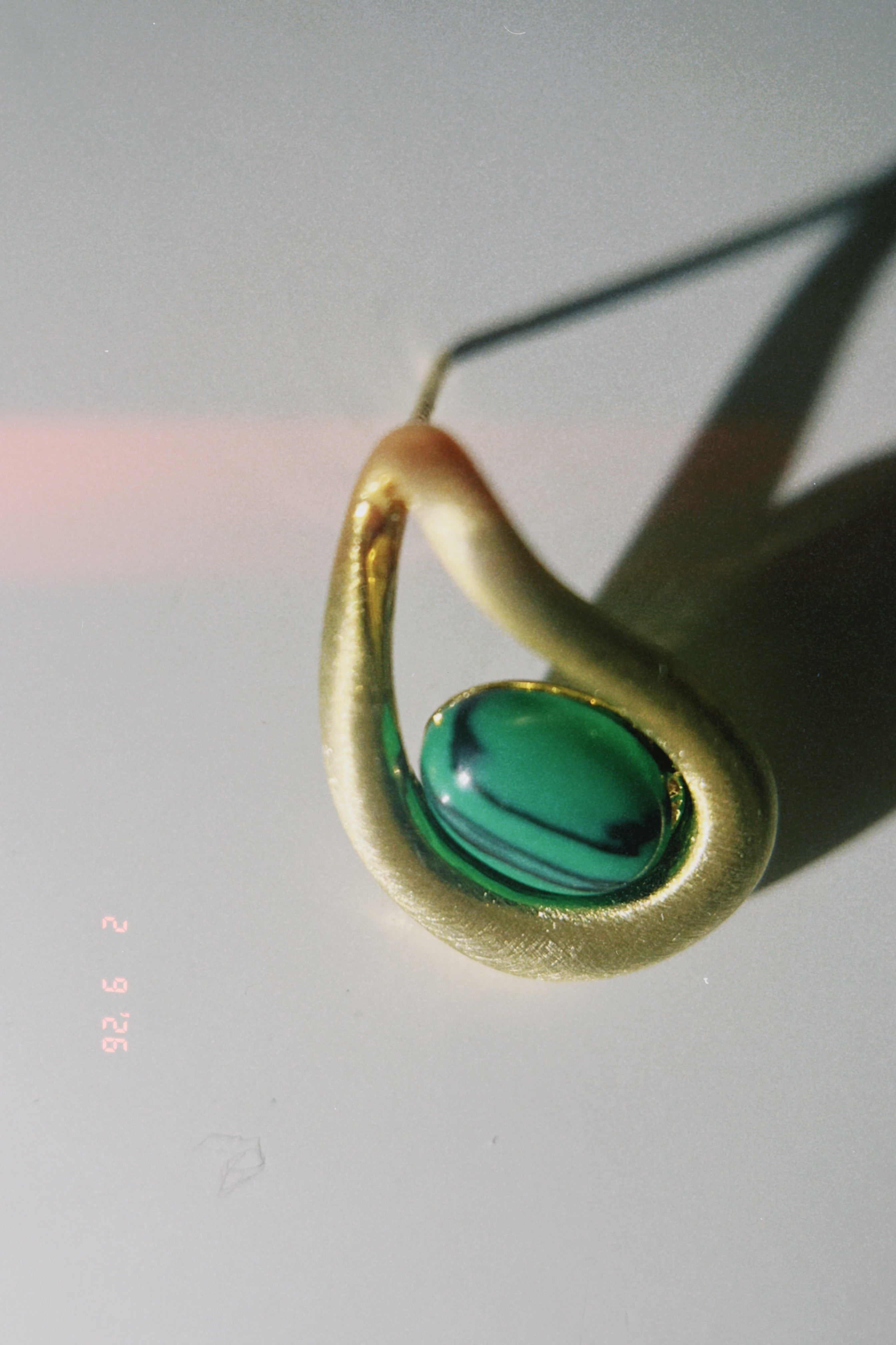 Gold earring with a green gemstone on a light gray background
