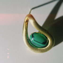 Gold earring with a green gemstone on a light gray background