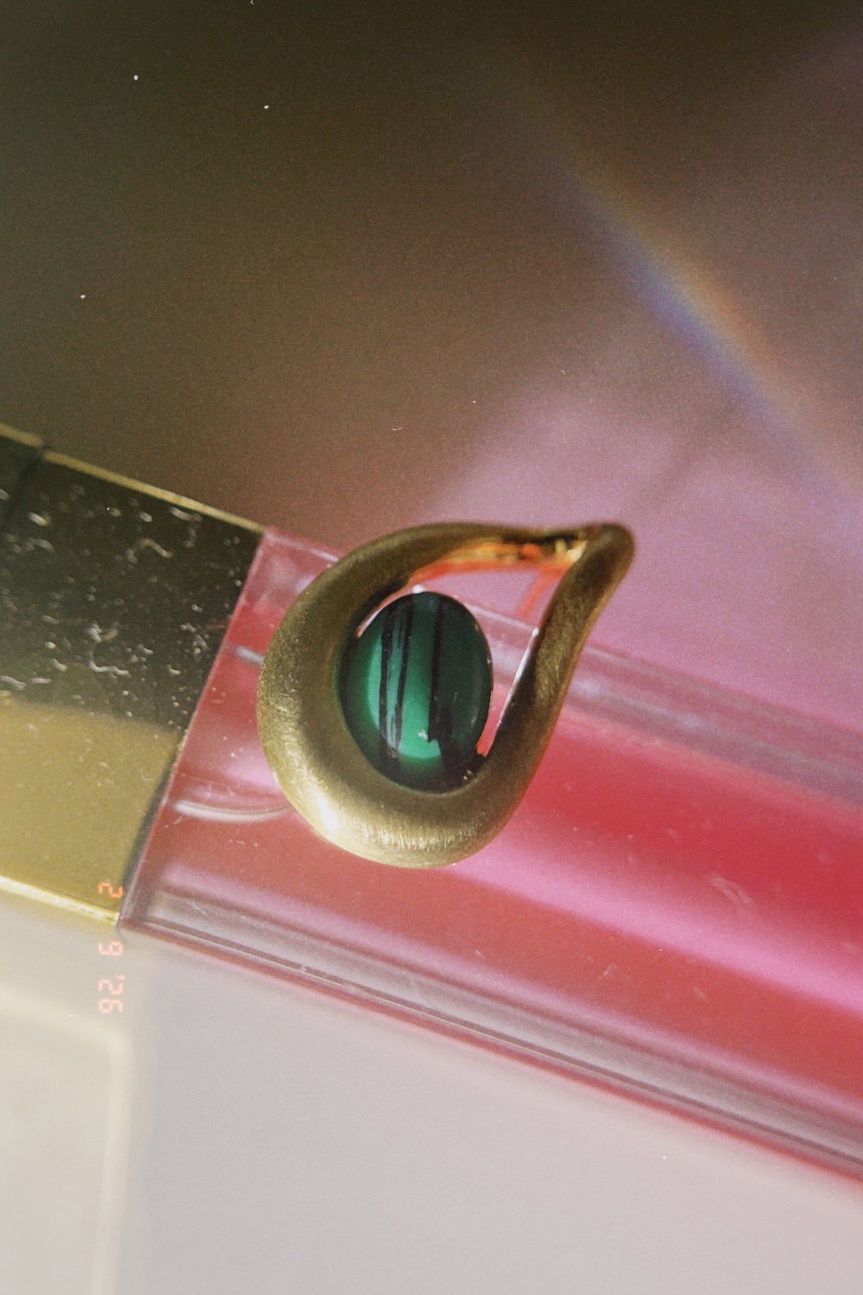 Gold earring with a green gemstone on a reflective surface