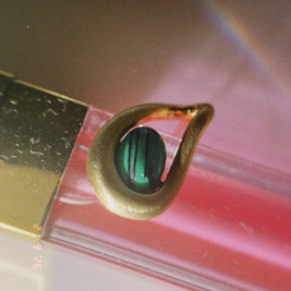 Gold earring with a green gemstone on a reflective surface