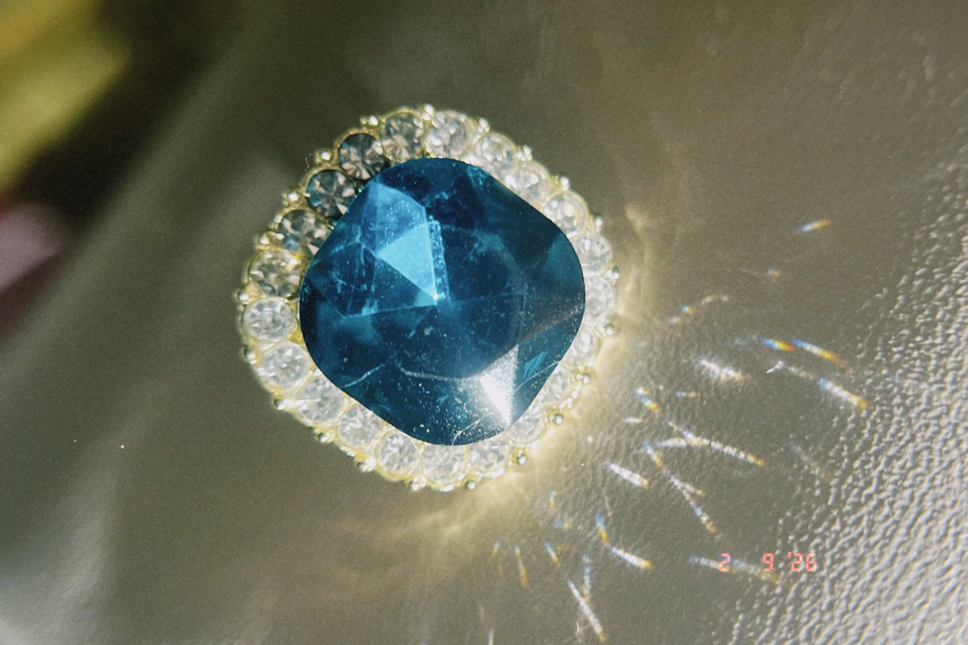 Blue gemstone ring with clear stones on a reflective surface
