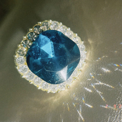 Blue gemstone ring with clear stones on a reflective surface