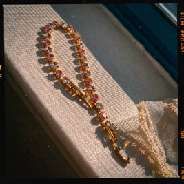 Someday she - American Honey dainty sunset pink and gold zircon bracelet on a textured surface, featuring a vintage film grain effect and dramatic warm sunlight shadows.