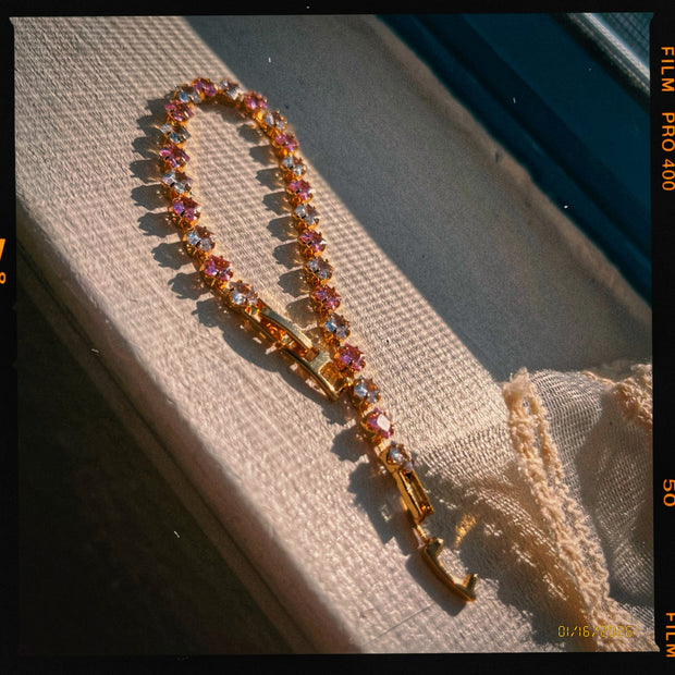 Someday she - American Honey dainty sunset pink and gold zircon bracelet on a textured surface, featuring a vintage film grain effect and dramatic warm sunlight shadows.