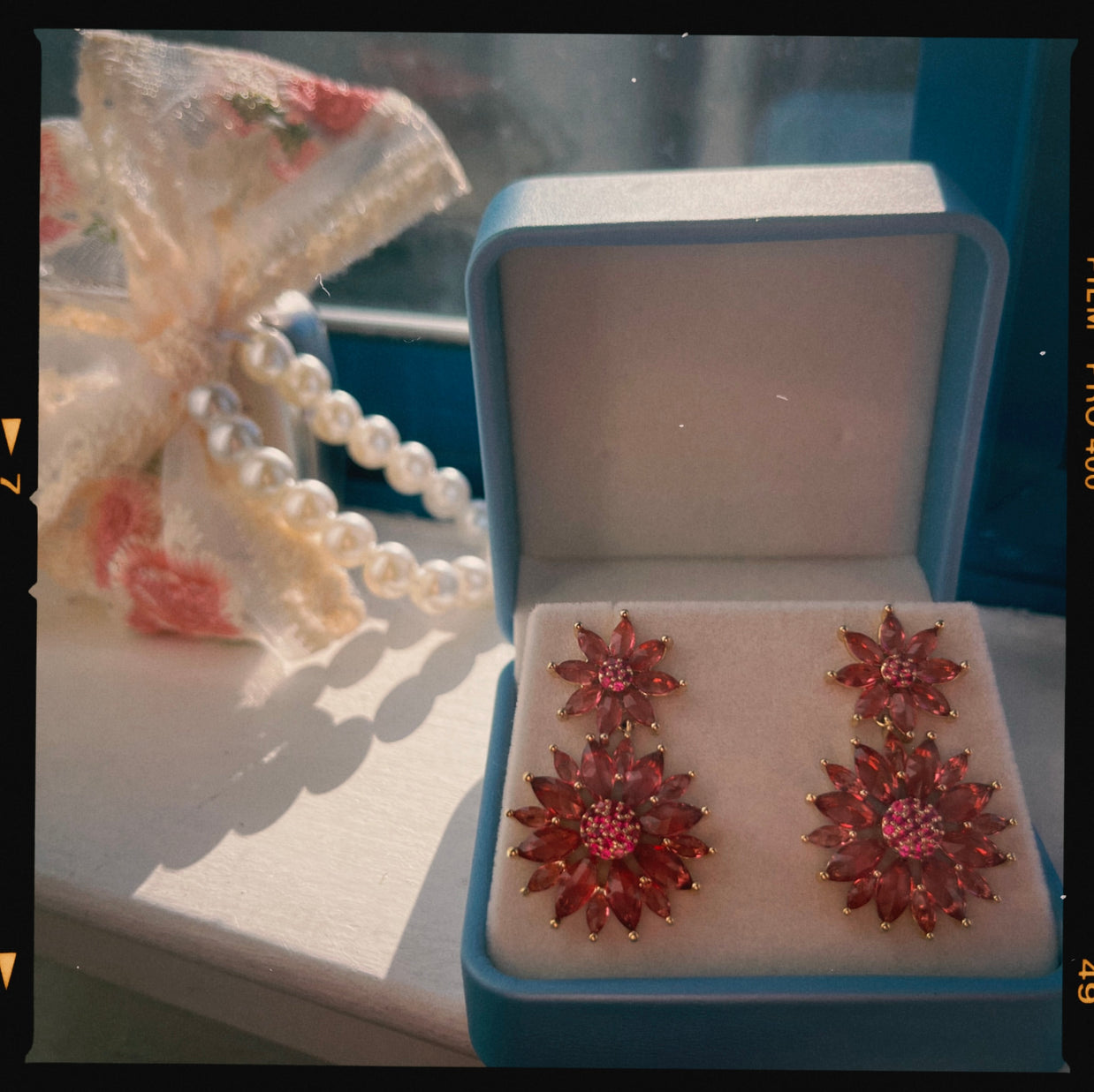 Red floral earrings in an open jewelry box with a pearl necklace in the background.