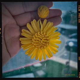 Yellow flower-shaped earring held in a hand with a blurred background