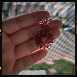 Hand holding a decorative pink flower earring against a screen door background