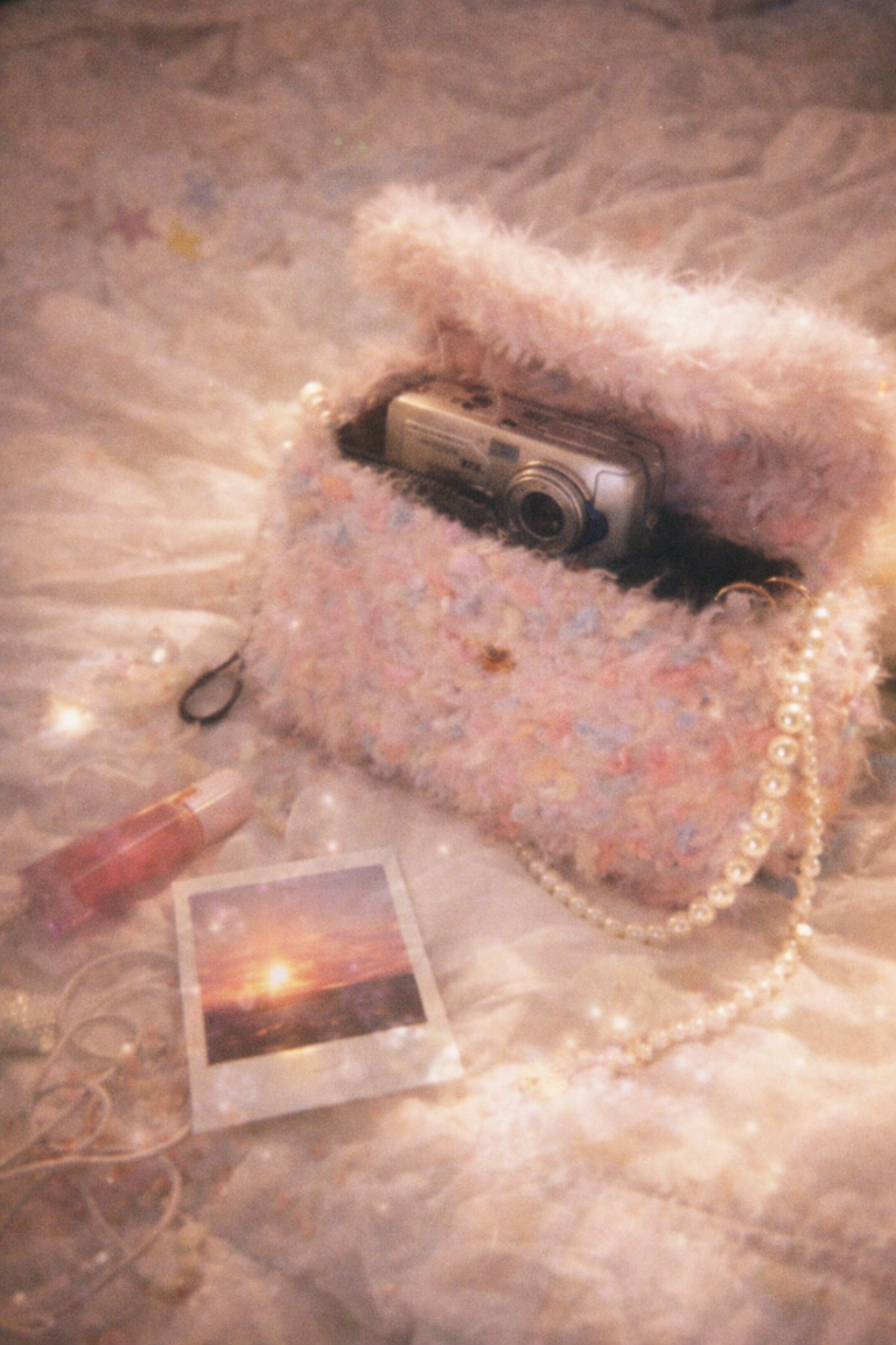 Someday she - Dream visual of the Deleted Scenes pink shaggy crochet bag on a soft dreamy surface, featuring a vintage digital camera and a sunset polaroid photo in an ethereal setting.