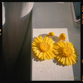 Someday she - Sunstroke natural raffia floral earrings in vibrant yellow, captured in bright direct sunlight on a textured gray surface with a vintage film border.