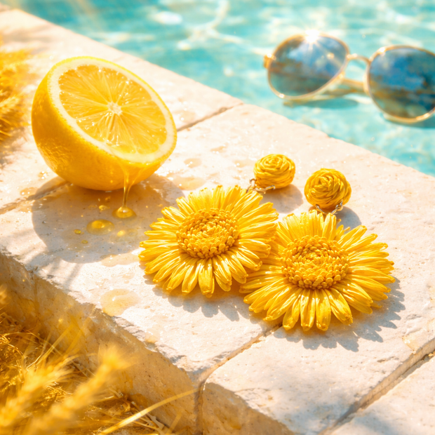 Someday she - Dream visual of yellow natural raffia floral earrings by a sparkling blue swimming pool, accompanied by a fresh lemon and sunglasses in bright summer sunlight.