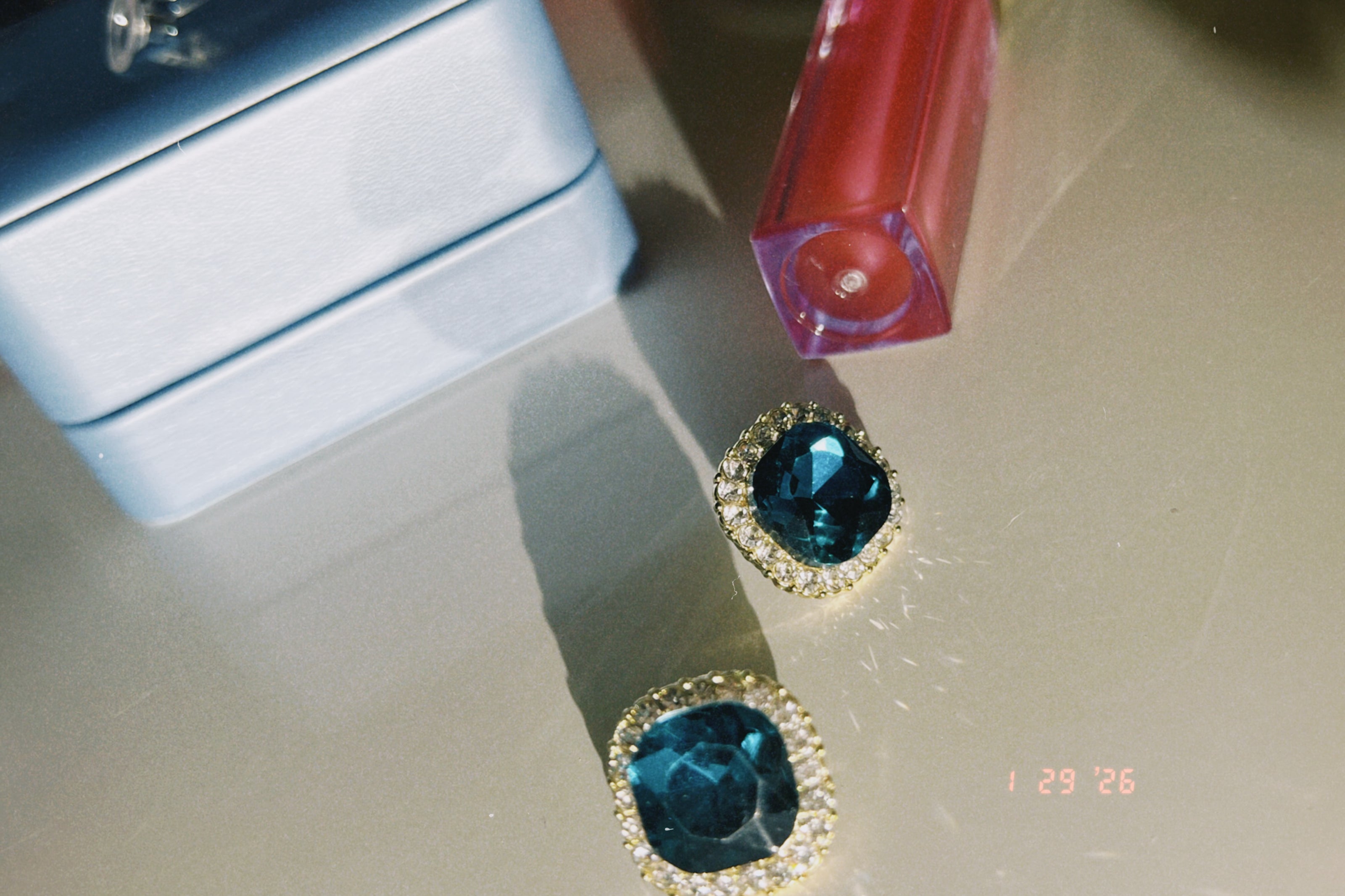 Someday she - The Blue Hour vintage-style square stud earrings featuring deep blue gemstones with a sparkling gold rim, resting on a reflective surface next to a light blue jewelry box.