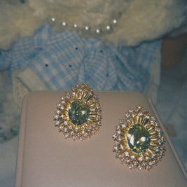 Someday she - The Green Library vintage emerald starburst halo statement studs, featuring deep green stones and a sparkling diamond-like halo on a beige cushion with a soft, retro film aesthetic.