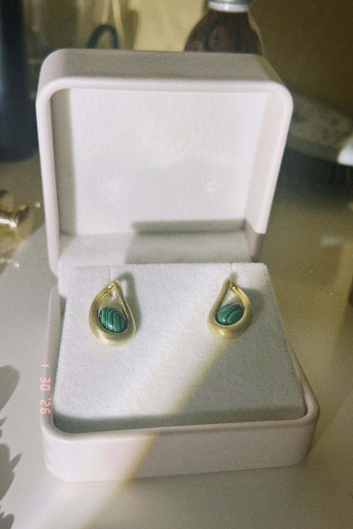 Someday she - The Green Light vintage-style gold drop earrings inlaid with green malachite stones, presented in a classic white jewelry box with soft dramatic lighting.