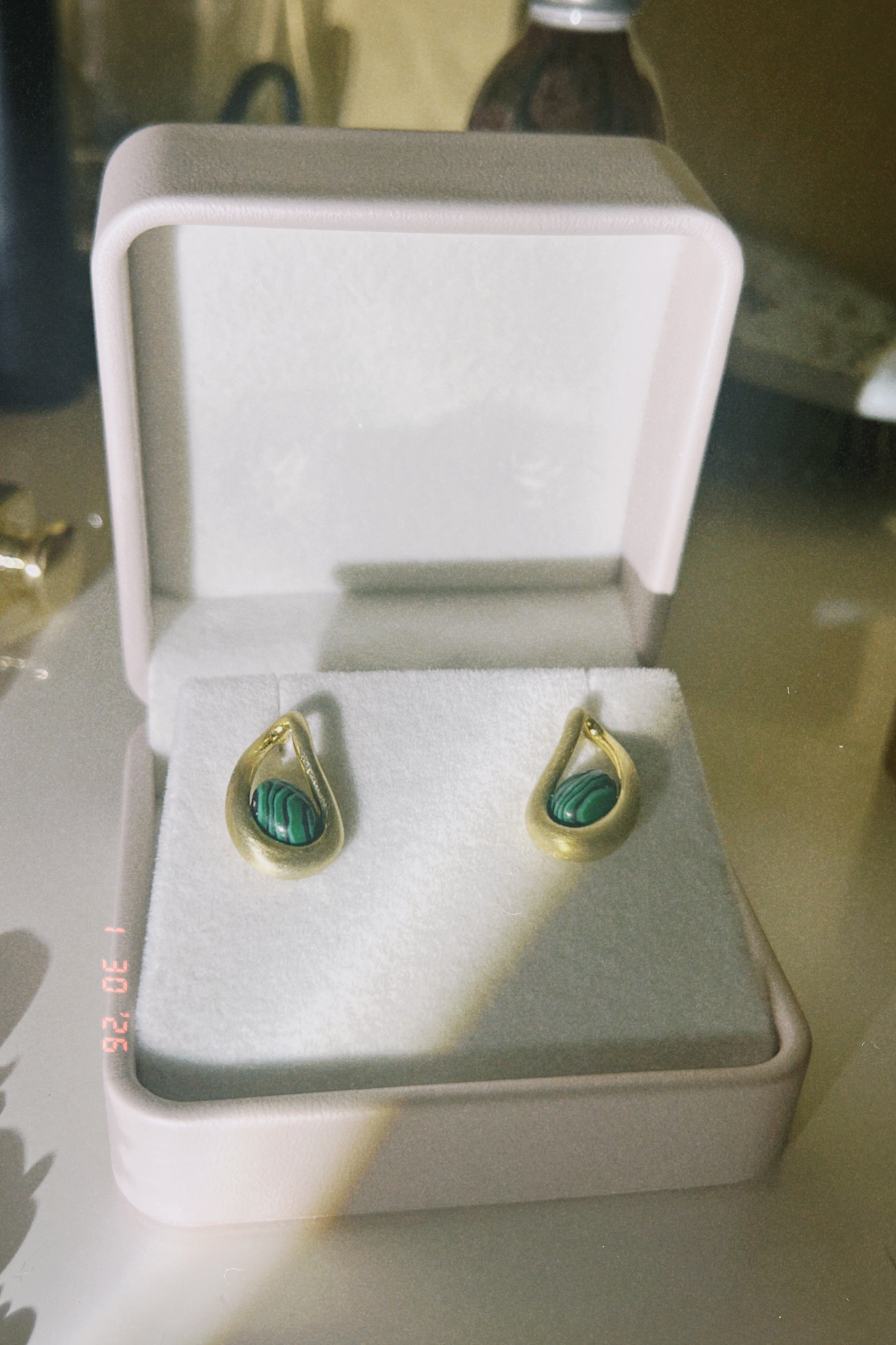 Someday she - The Green Light vintage-style gold drop earrings inlaid with green malachite stones, presented in a classic white jewelry box with soft dramatic lighting.
