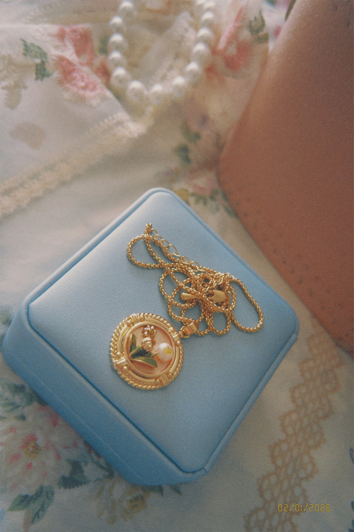 Someday she - The Love Letter French vintage relief floral medallion necklace in gold, resting on a light blue jewelry box with a delicate floral lace and pearl backdrop.