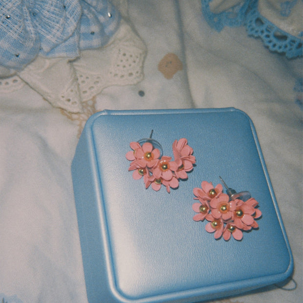 Someday she - The Strawberry Dream petite pink floral stud earrings with gold centers, resting on a vintage light blue jewelry box against a delicate patterned lace background.