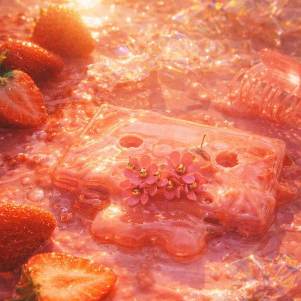Someday she - Dream visual of The Strawberry Dream pink floral stud earrings resting on a translucent pink cassette tape, surrounded by fresh strawberries in a shimmering, nostalgic pink liquid.